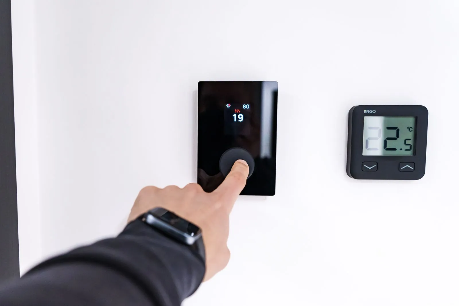 A hand pressing the dial of a wall-mounted smart thermostat