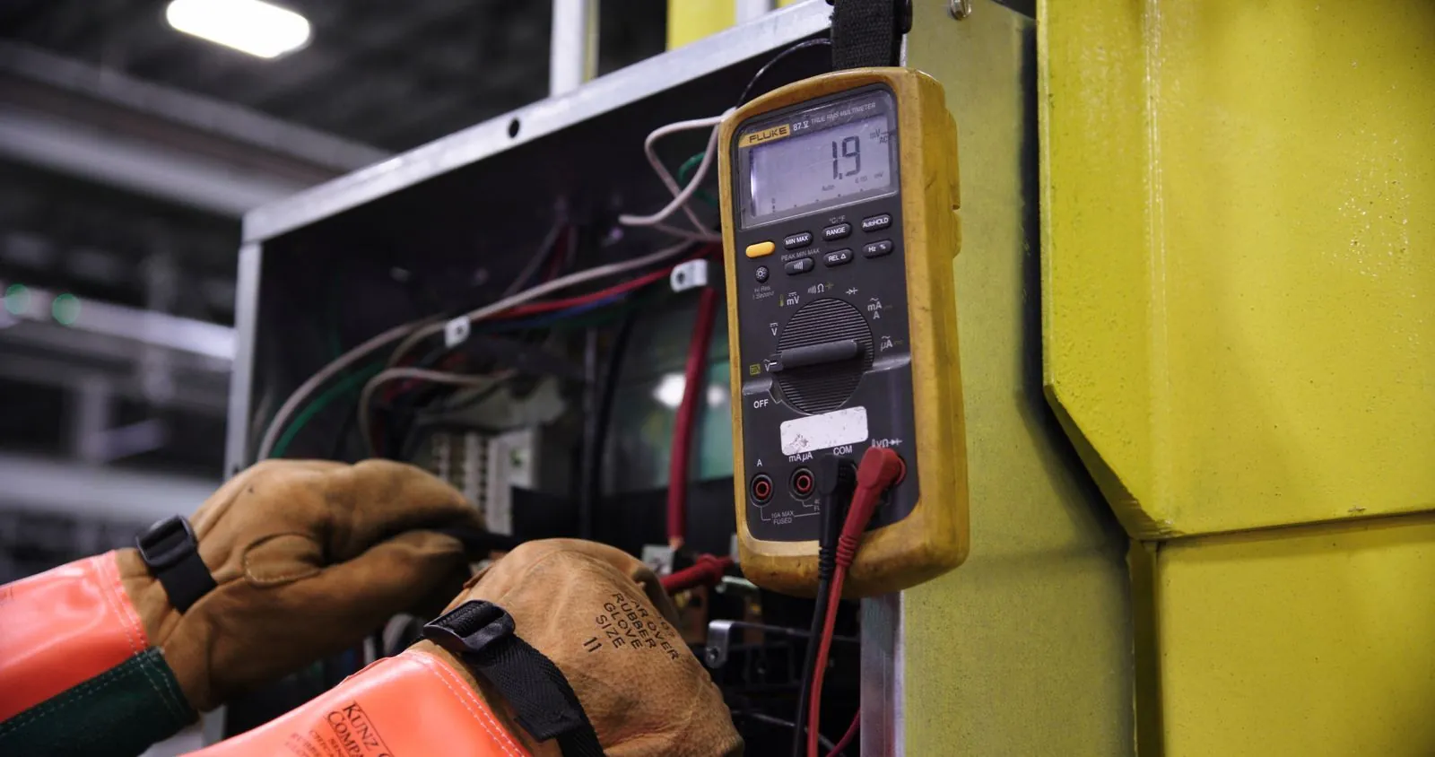 Gloved hands testing control-panel wiring with a digital multimeter