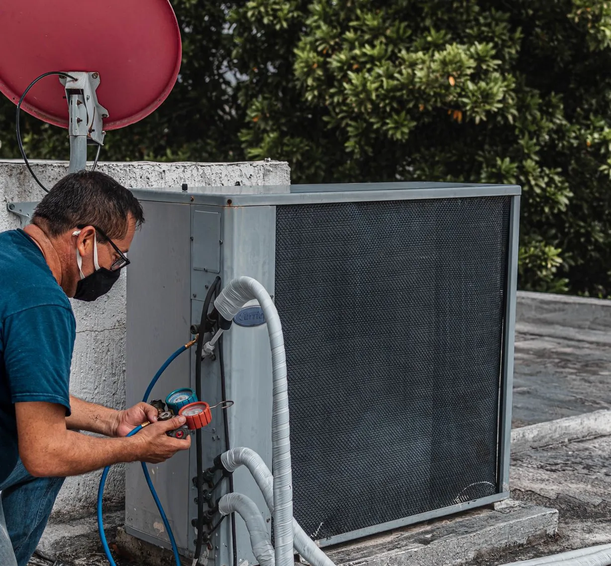 Technician holding a refrigerant gauge manifold connected to the service ports of an outdoor condensing unit