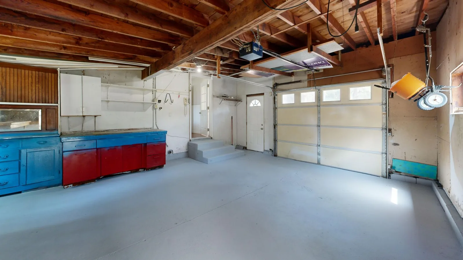 Inside a two-car garage: a sectional garage door with windows, storage cabinets and a bare concrete floor